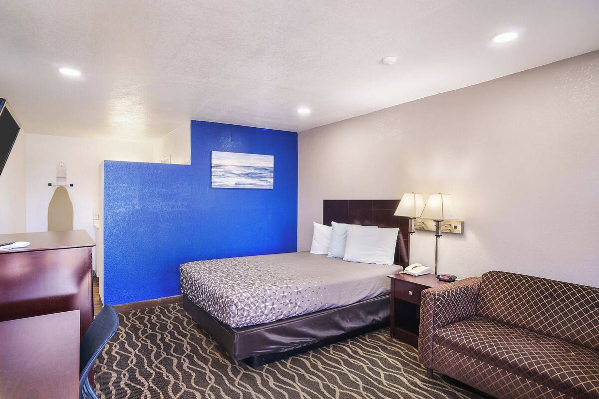 Une chambre d’hôtel avec un lit, un bureau, une chaise, un canapé et une lampe.
