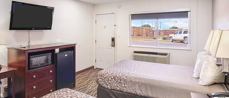 Habitación de hotel con dos camas, televisión, escritorio, microondas y ventana con vista a la calle.