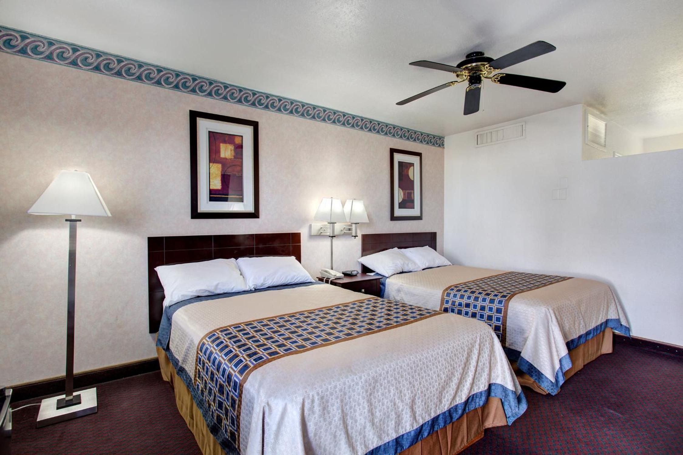 A hotel room with two beds, a ceiling fan, and two wall-mounted lamps.