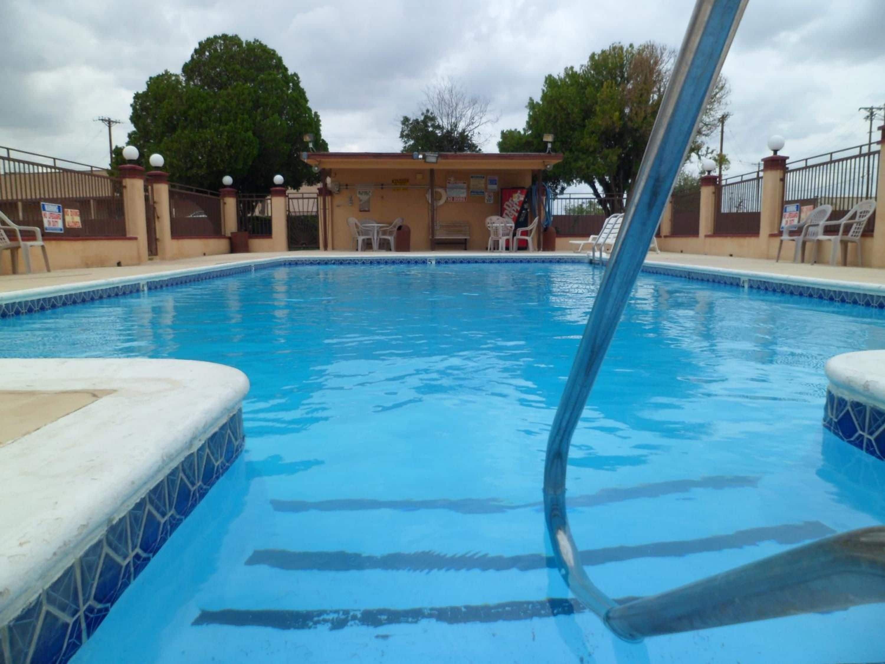 Una piscina con borde de azulejos, un área techada con sillas y una valla.