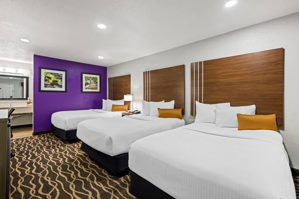 Ein Hotelzimmer mit drei Betten, violetten Wänden und Holz-Kopfteilen.