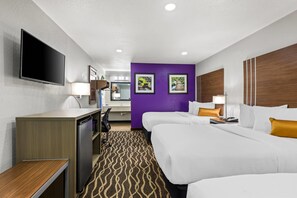 A hotel room with two beds, a desk, a television, and a bathroom visible through an open door.