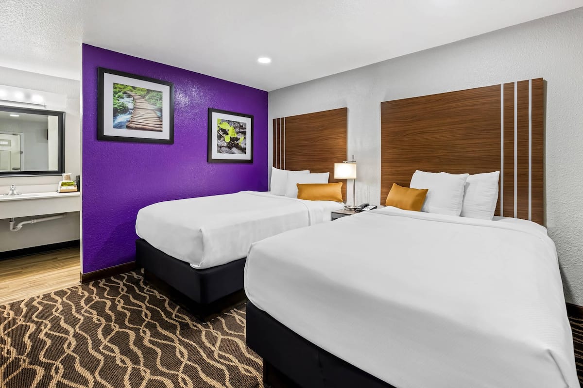 Ein Hotelzimmer mit zwei Betten, einer violetten Akzentwand, einem Holzkopfende und einem gemusterten Teppich.
