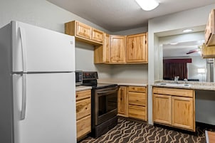 Una cocina compacta con refrigerador, estufa, microondas, gabinetes de madera y piso con diseño.