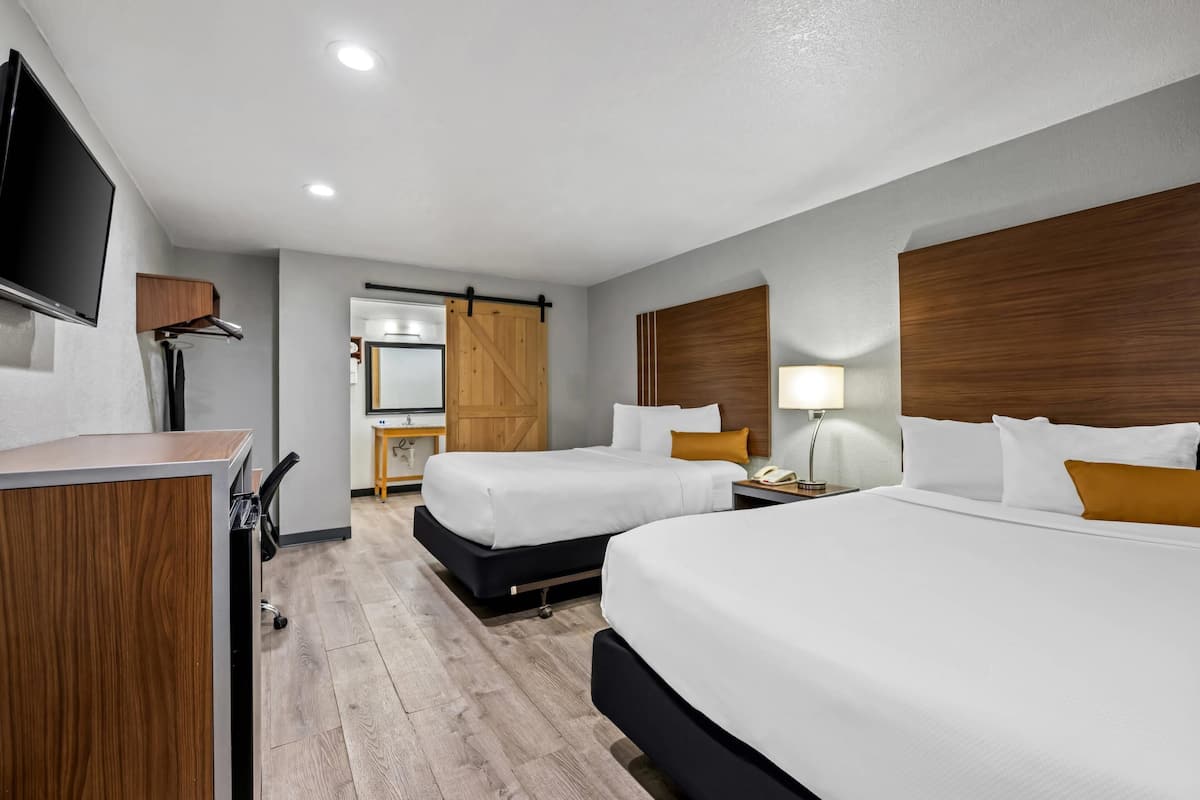 Ein Hotelzimmer mit zwei Betten, einem Schreibtisch, einem Fernseher und einem hölzernen Kopfteil.
