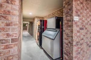 Un pasillo con paredes de ladrillo, una máquina expendedora y un refrigerador.