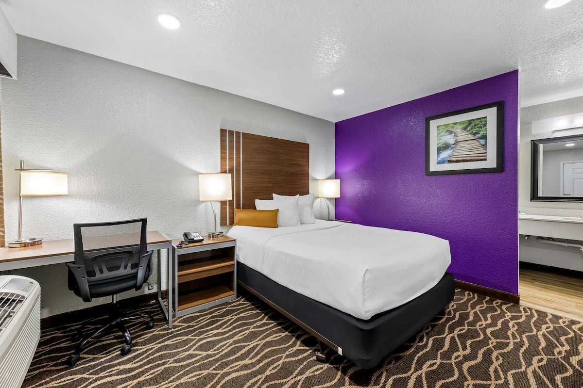 Ein Hotelzimmer mit Bett, Schreibtisch, Stuhl und einer Wand in Lila.