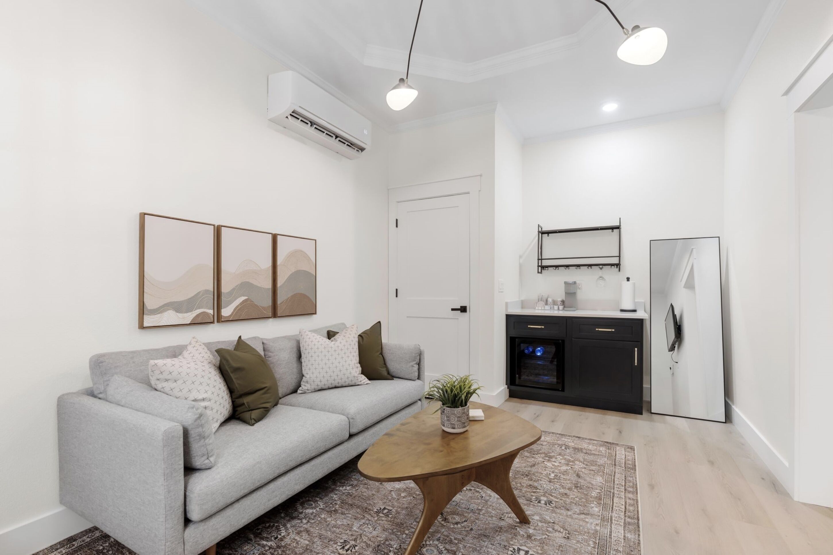 A modern living room with a grey sofa, a wooden coffee table, and a kitchen area with a refrigerator and stove.