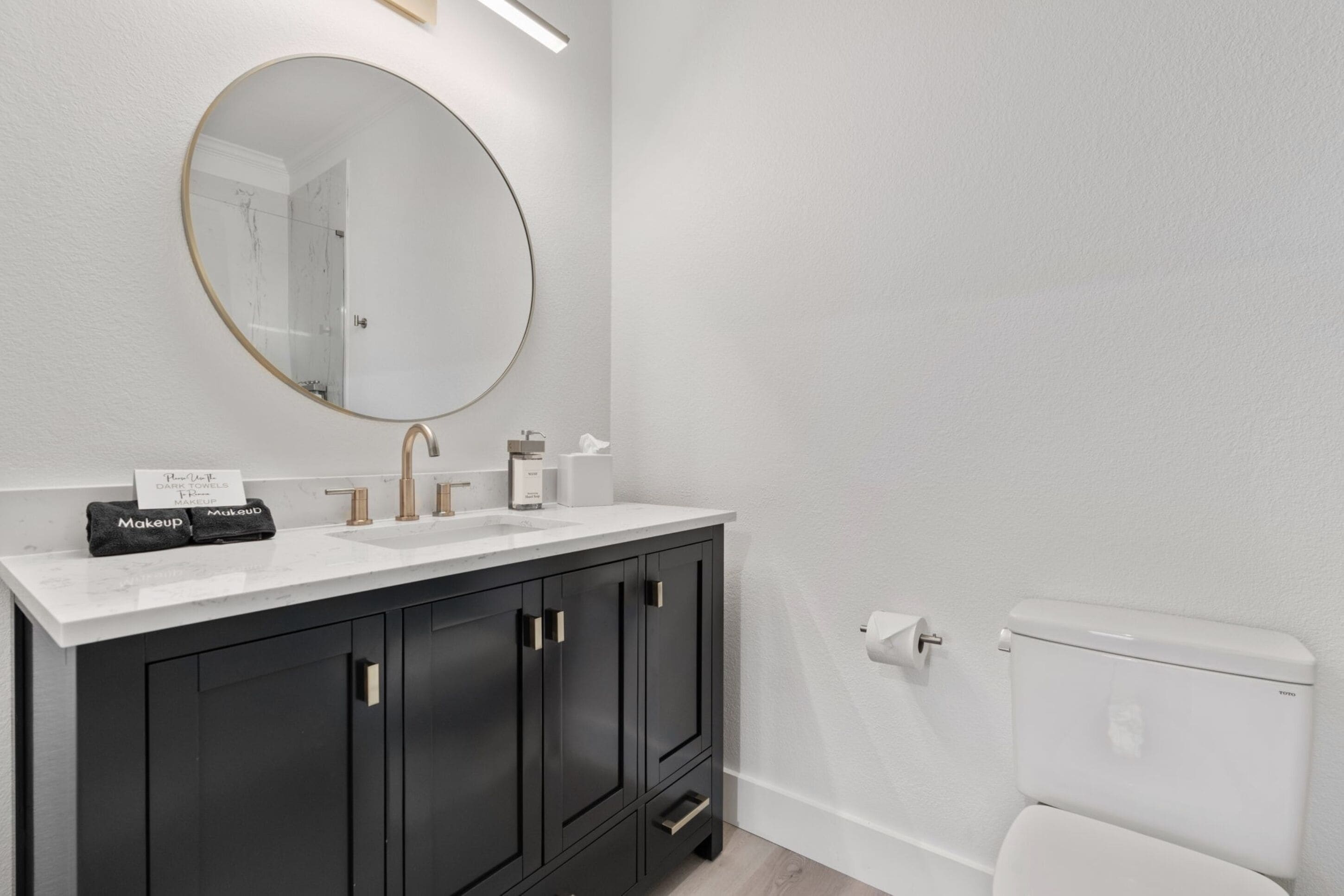 Un baño moderno con un espejo redondo, un lavabo blanco, armarios negros y un inodoro blanco.
