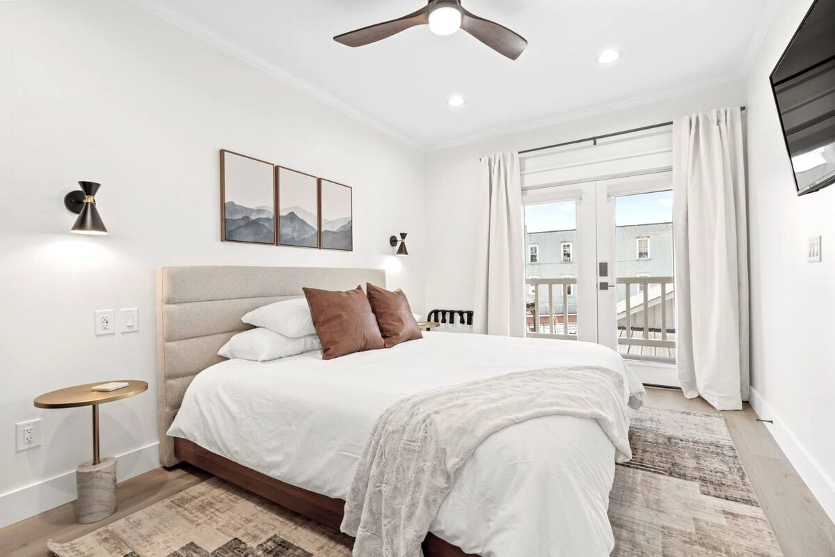 Quarto com cama grande, ventilador de teto, televisão na parede e janela com cortinas.