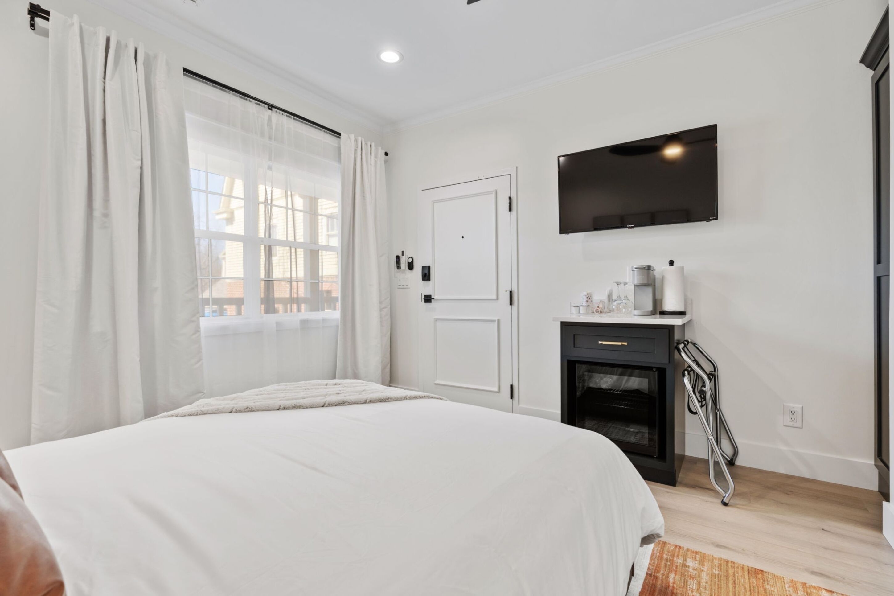 A modern bedroom with a large bed, a television mounted on the wall, a fireplace, and a window with curtains.