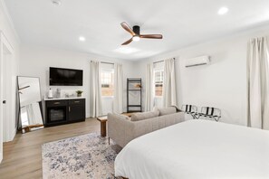 Una habitación de hotel moderna con una cama grande, un sofá, un televisor, un ventilador de techo y una pequeña mesa con una planta.