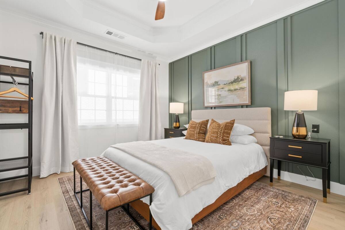 Quarto com uma cama grande, duas mesas de cabeceira com luminárias, um banco, um guarda-roupa e uma janela com cortinas.