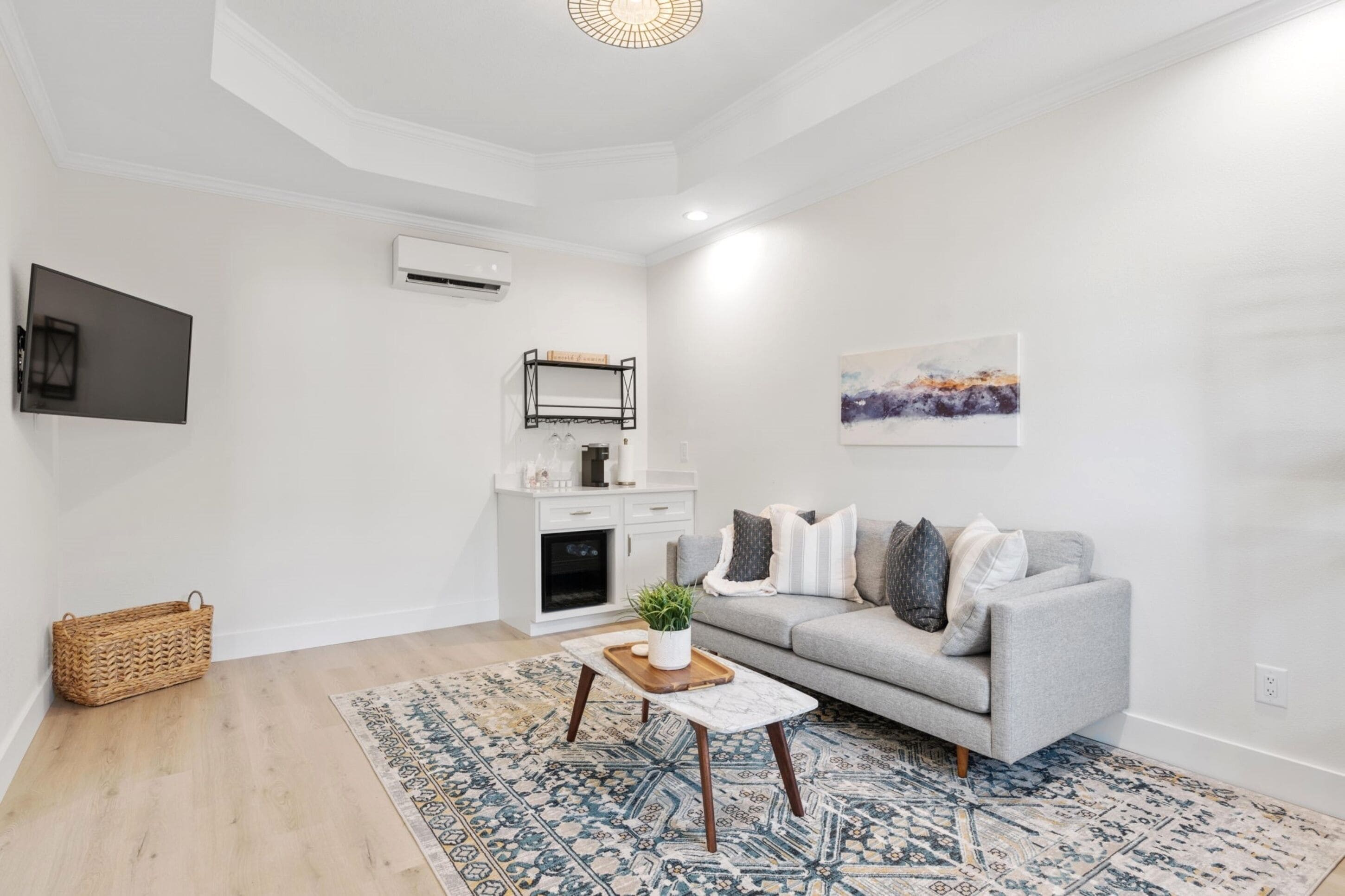 A modern living room with a grey sofa, a coffee table, a patterned rug, a flat-screen TV, and a fireplace.