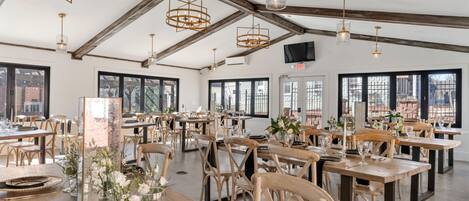 A spacious dining area with wooden tables and chairs, large windows, and hanging pendant lights.