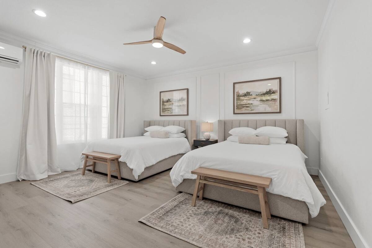 Quarto moderno com duas camas, ventilador de teto e obras de arte nas paredes.