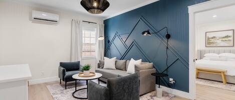 Una sala de estar moderna con una pared azul de acento, un sofá gris, un sillón negro y una mesa de centro redonda.