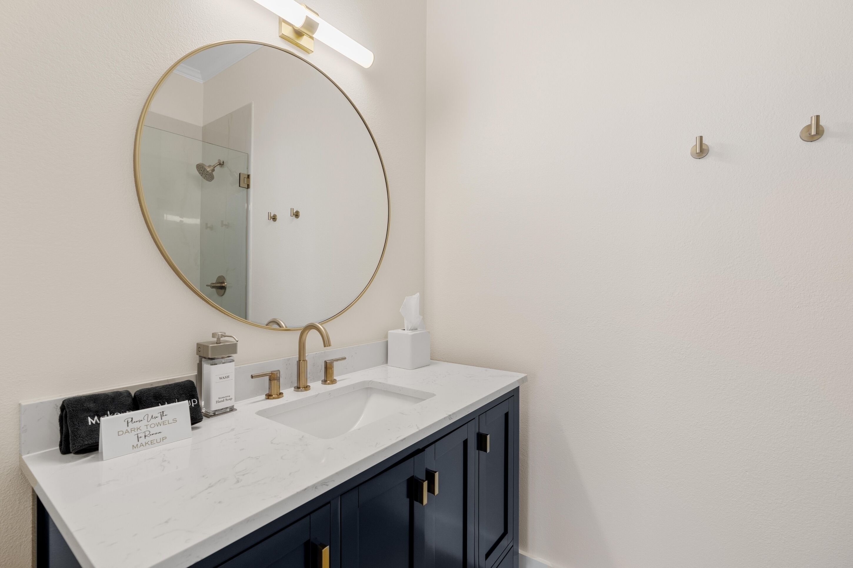 A bathroom with a round mirror, a white sink, and dark cabinets.