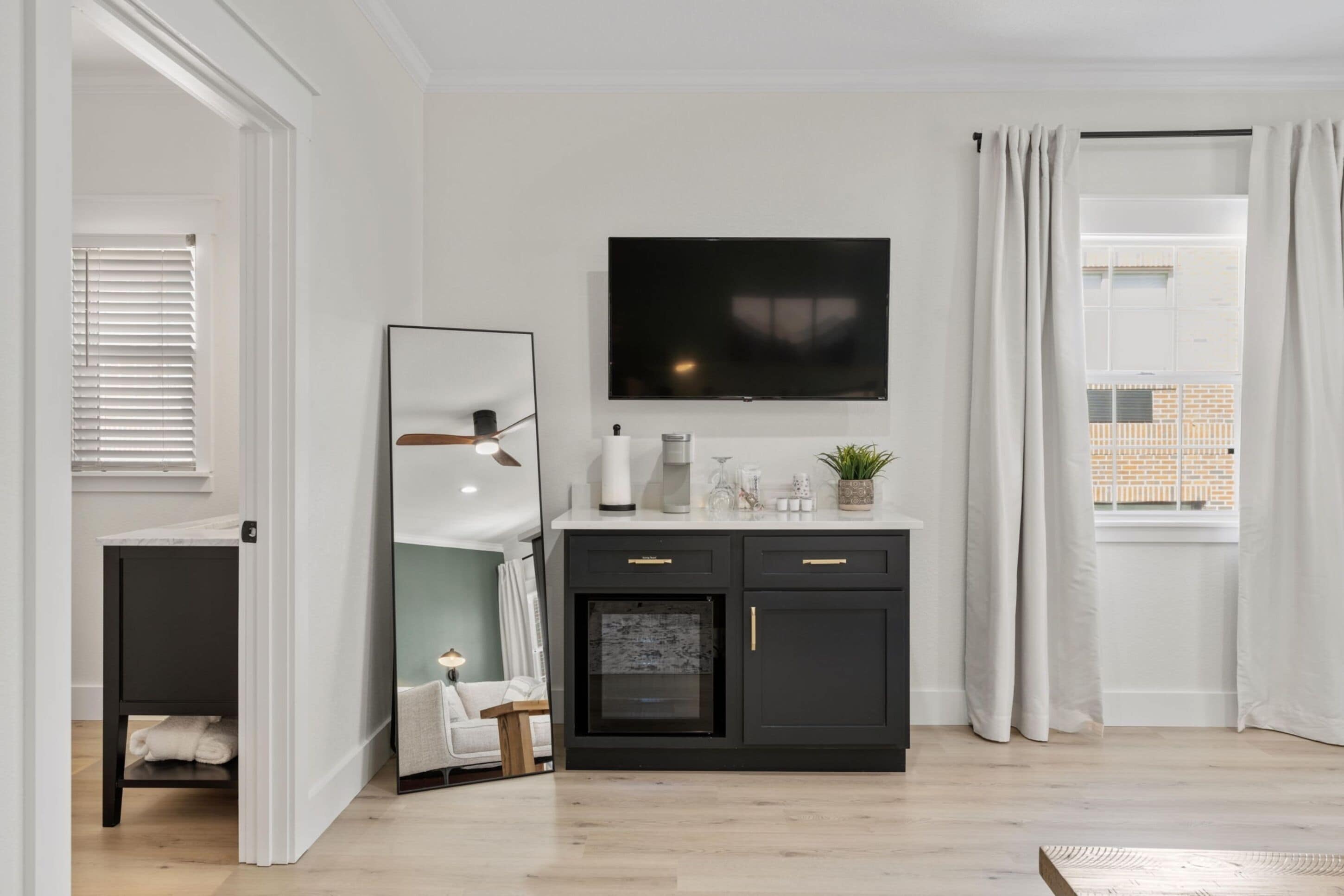 A modern living room with a black entertainment unit, a flat-screen TV, and a large mirror.
