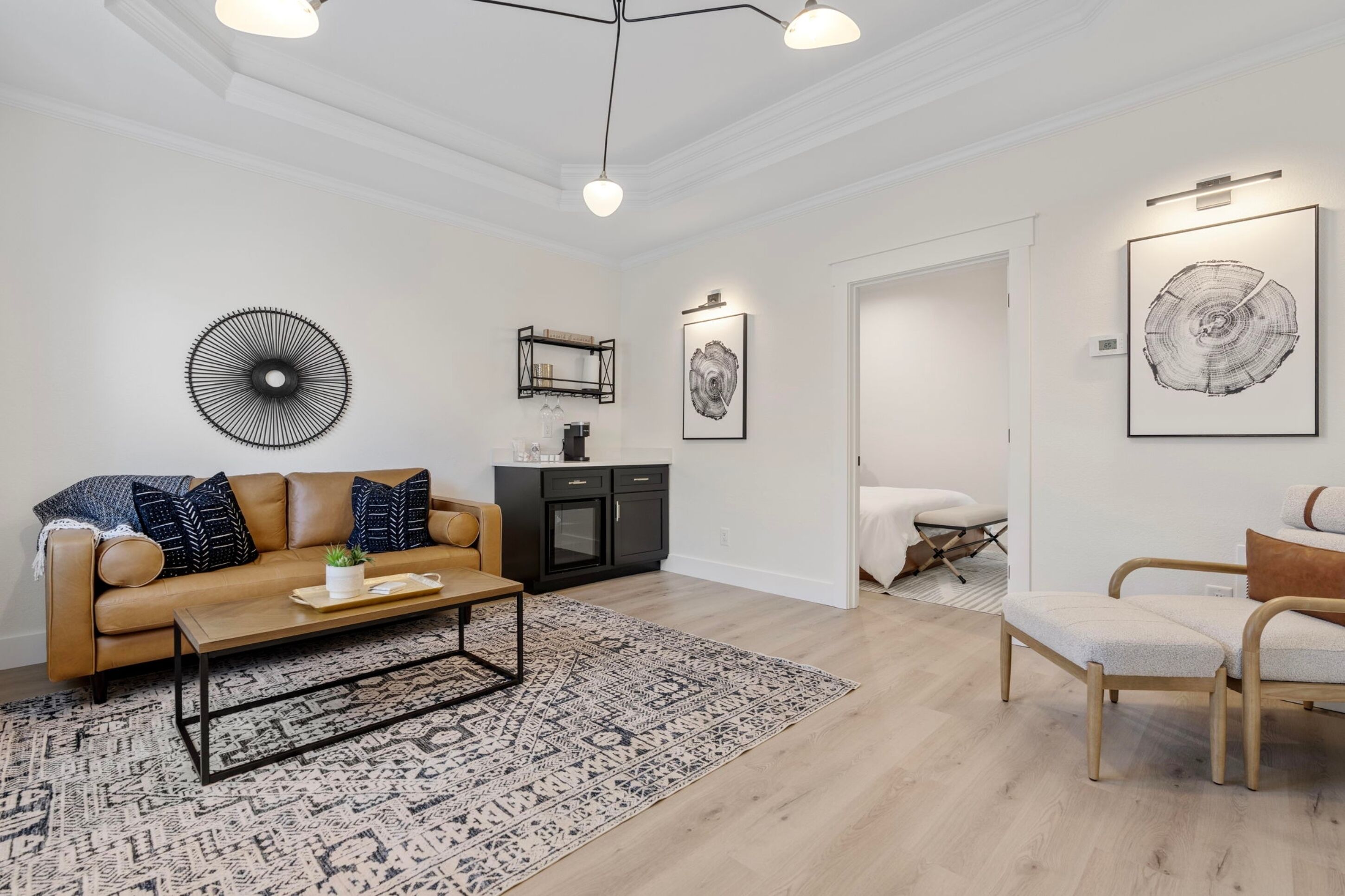 A modern living room with a beige sofa, a coffee table, and a patterned rug. There is a black cabinet and a framed artwork on the wall.