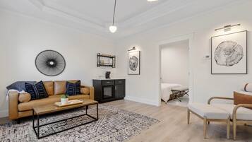 A modern living room with a beige sofa, a coffee table, and a patterned rug. There is a black cabinet and a framed artwork on the wall.