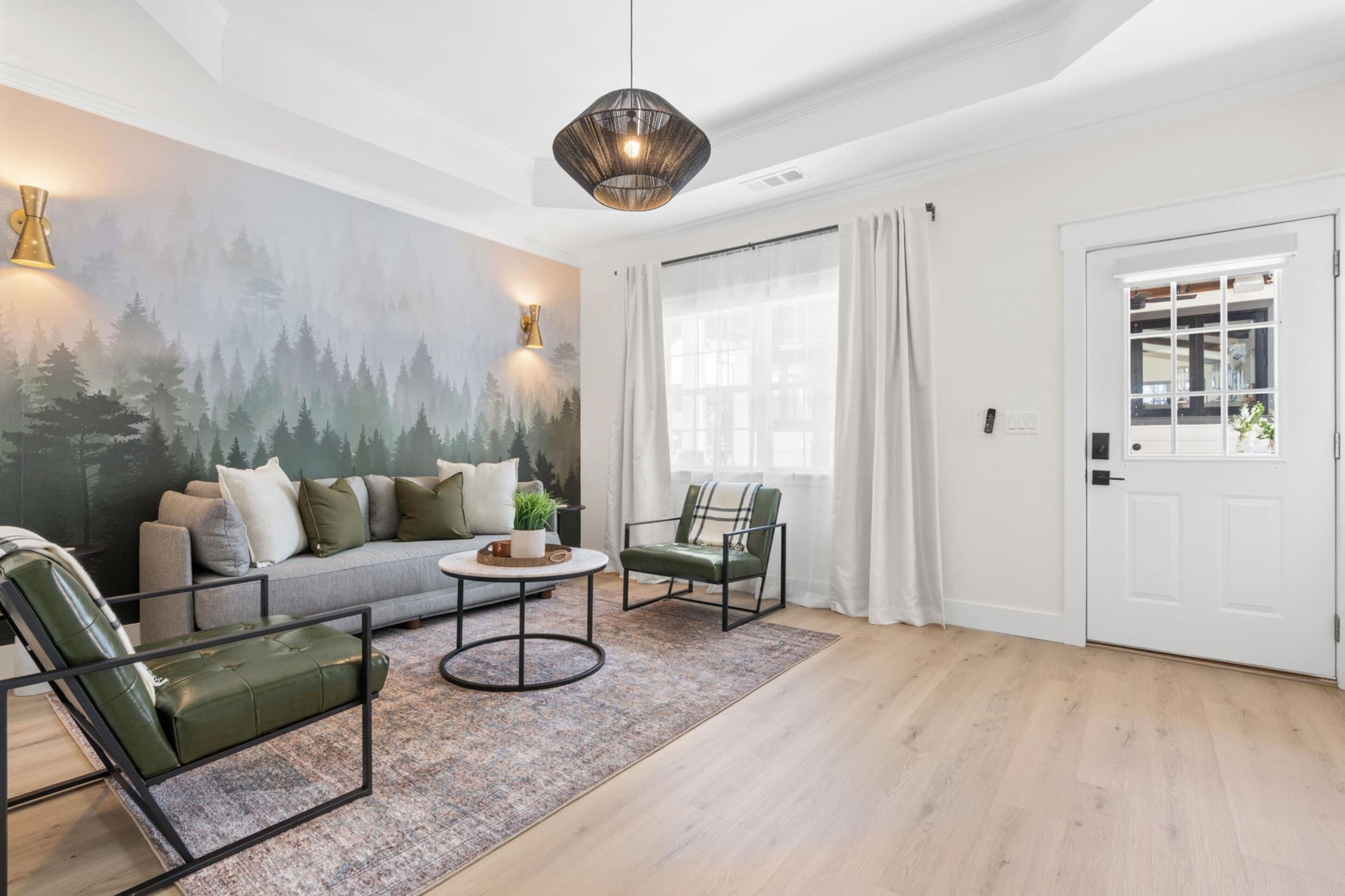 A modern living room with a sofa, two armchairs, a coffee table, and a forest mural on the wall.