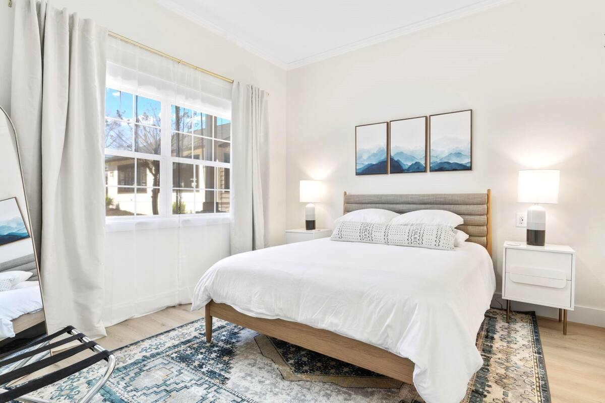 Quarto moderno com uma cama grande, mesa de cabeceira, abajur e vista para o exterior pela janela.