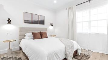 Een moderne slaapkamer met een groot bed, twee nachtkastjes, een hoofdbord en een raam met dunne gordijnen.