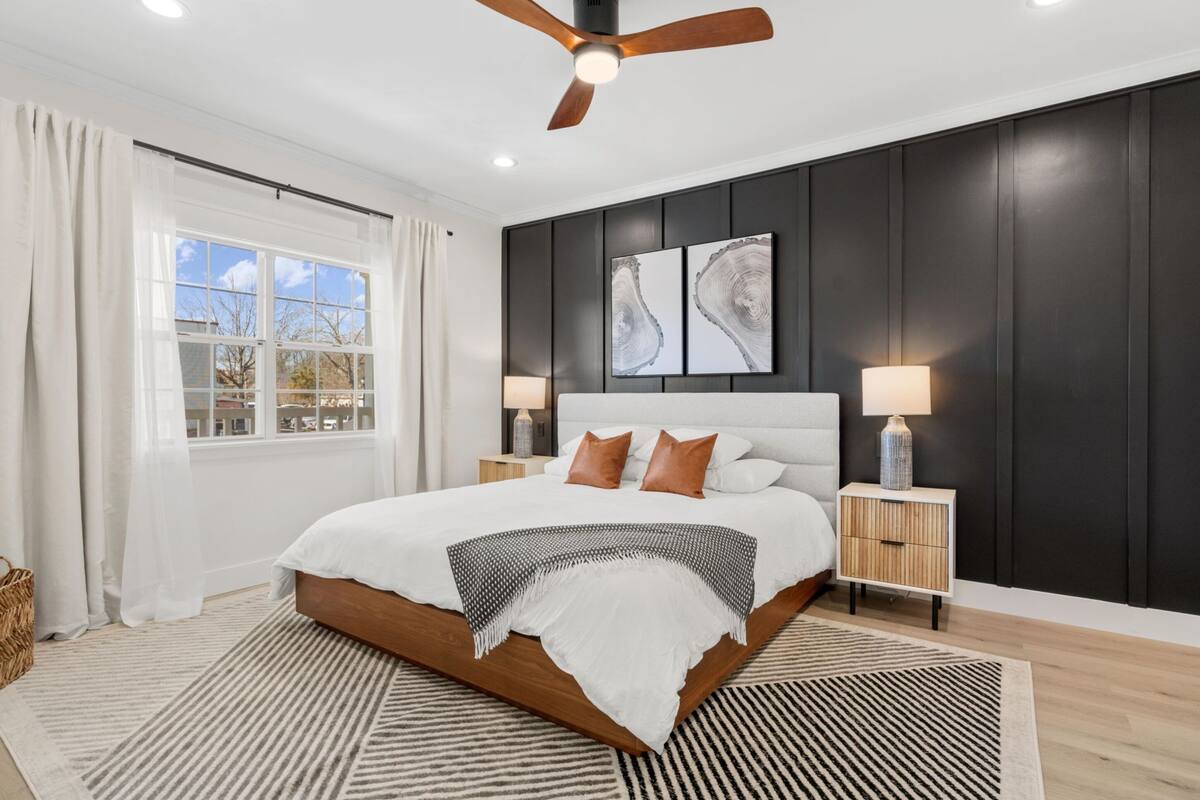 Quarto com uma cama grande, duas mesas de cabeceira com luminárias, um ventilador de teto e uma janela com cortinas.