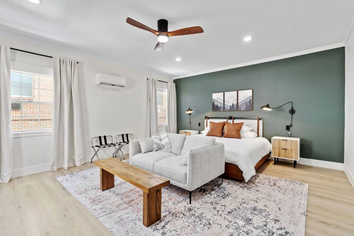 Quarto moderno com cama, sofá, banqueta e ventilador de teto.