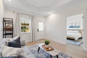 Una sala moderna con un sofá, una mesa de centro con una planta y vista a un dormitorio a través de una puerta abierta.