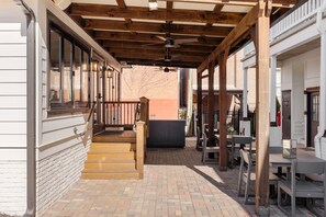 Un área de patio techada con vigas de madera, ventilador de techo y mobiliario exterior.