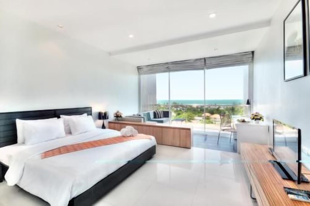 Un dormitorio moderno con una cama grande, un banco de madera, un televisor y un balcón con vistas.