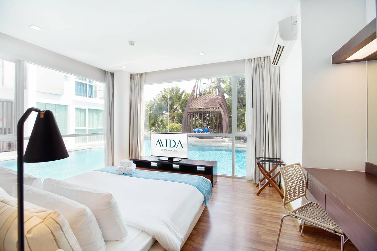 Una habitación de hotel con una cama grande, televisión, vista a una piscina y una silla.