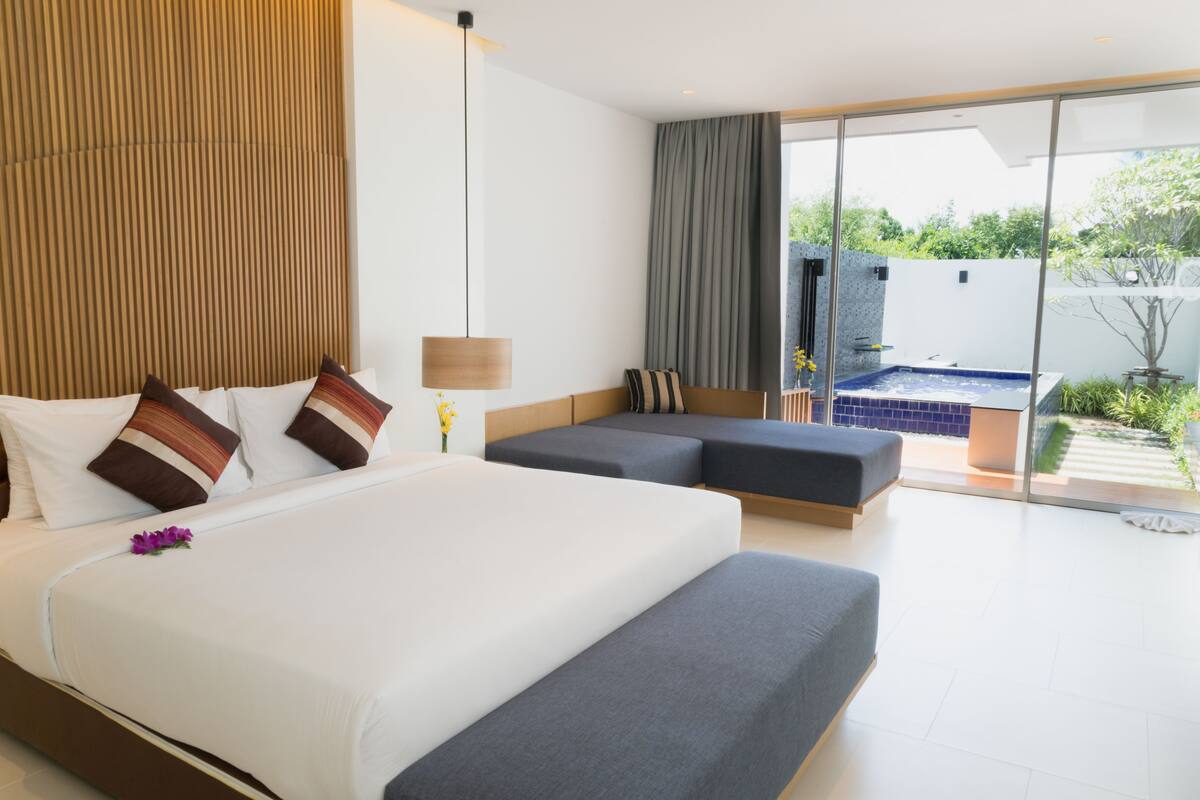 Una habitación de hotel moderna con una cama grande, zona de estar y vistas a una piscina.