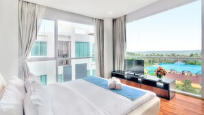 A modern hotel room with a large bed, a TV on a wooden console, and a balcony with a view of a swimming pool and buildings. - Mida De Sea Hua Hin (Cha-am)
