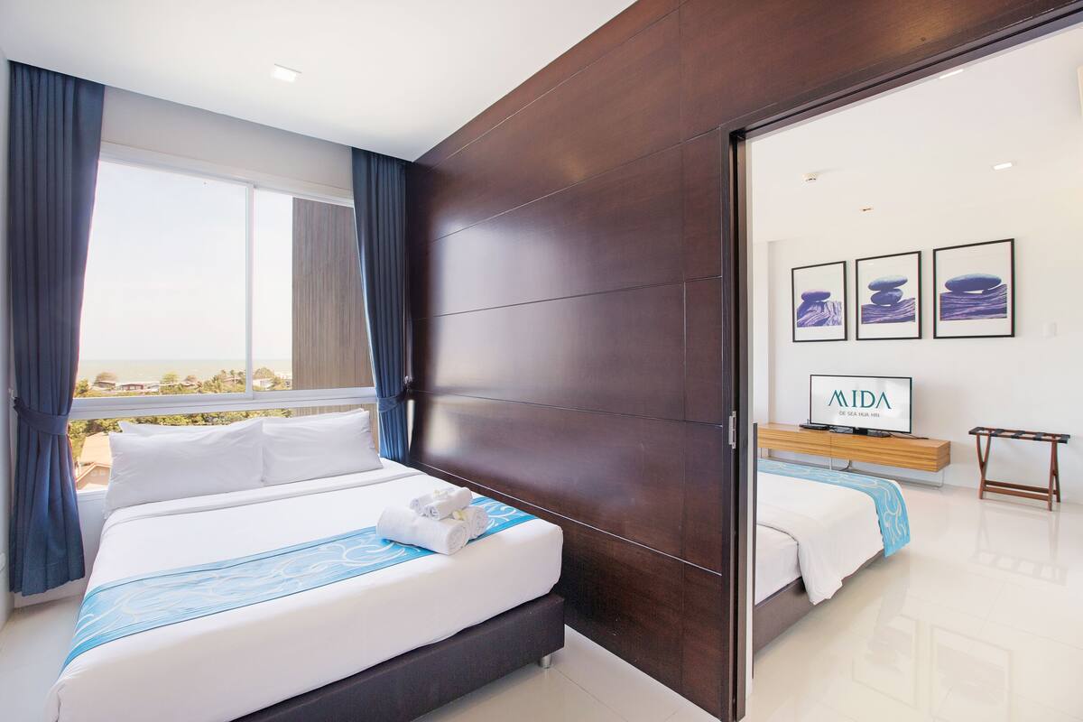 Una habitación de hotel moderna con una cama grande, vistas de la ciudad y un televisor sobre un soporte de madera.