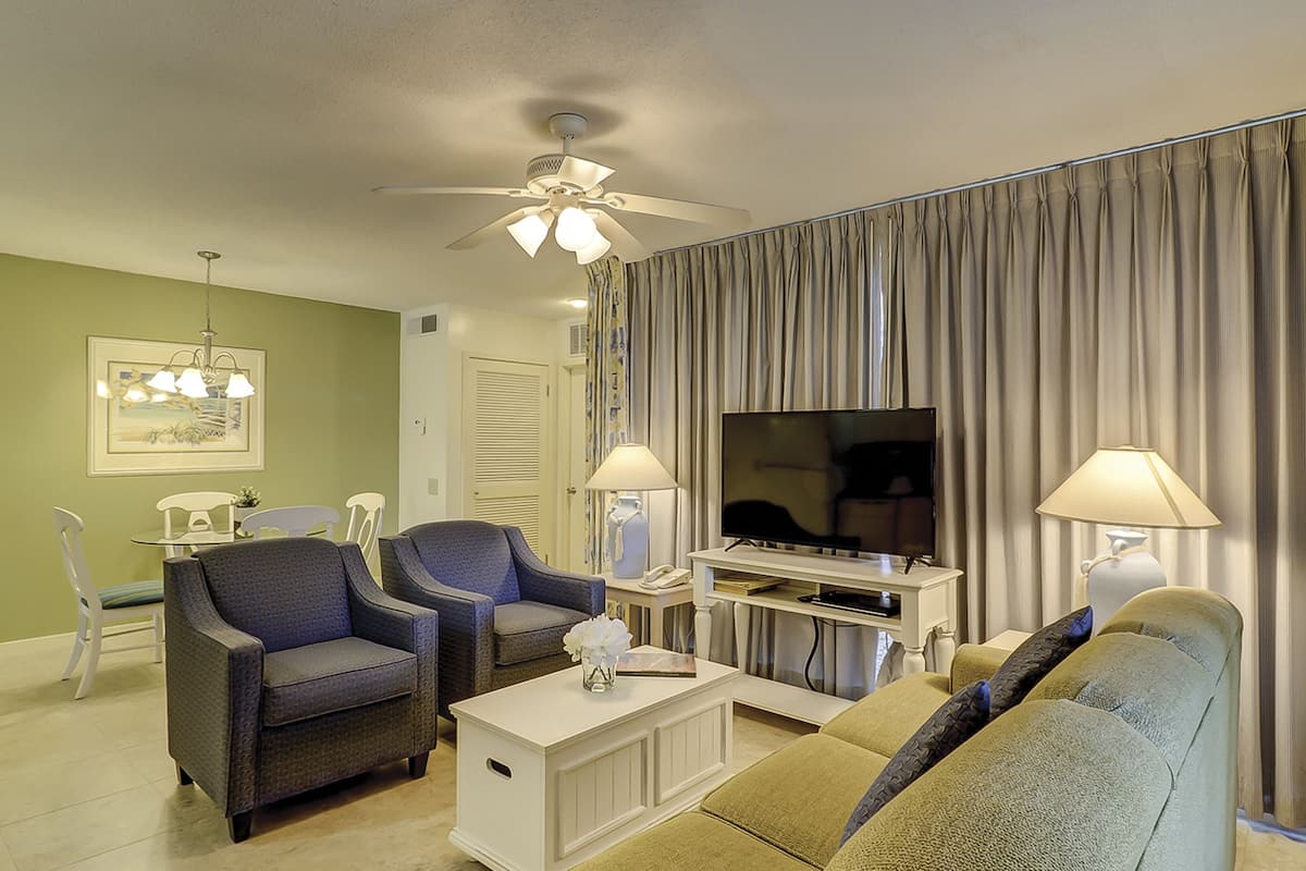 Een woonkamer met twee fauteuils, een bank, een televisie en een plafondventilator.