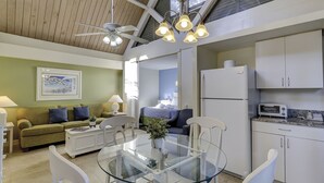 A modern kitchen with white cabinets, a built-in microwave, and a toaster. There is a dining area with a glass table and chairs, and a ceiling fan above. - The Village At Palmetto Dunes (Hilton Head Island)