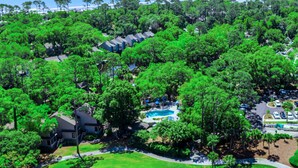 A golf course with a swimming pool, surrounded by dense greenery and a parking area. - The Village At Palmetto Dunes (Hilton Head Island)