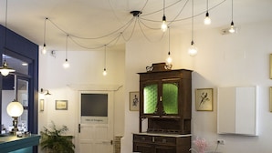 A spacious living area with a herringbone wood floor, a blue sofa, two wicker chairs, a small round table with a vase, and a cabinet with a green glass door. - Hospedium Hotel Maestrazgo de Calatrava (Almagro)