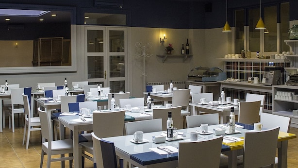 A well-lit dining area with multiple tables and chairs, a ceiling fan, and a kitchen area in the background. - Hospedium Hotel Maestrazgo de Calatrava (Almagro)