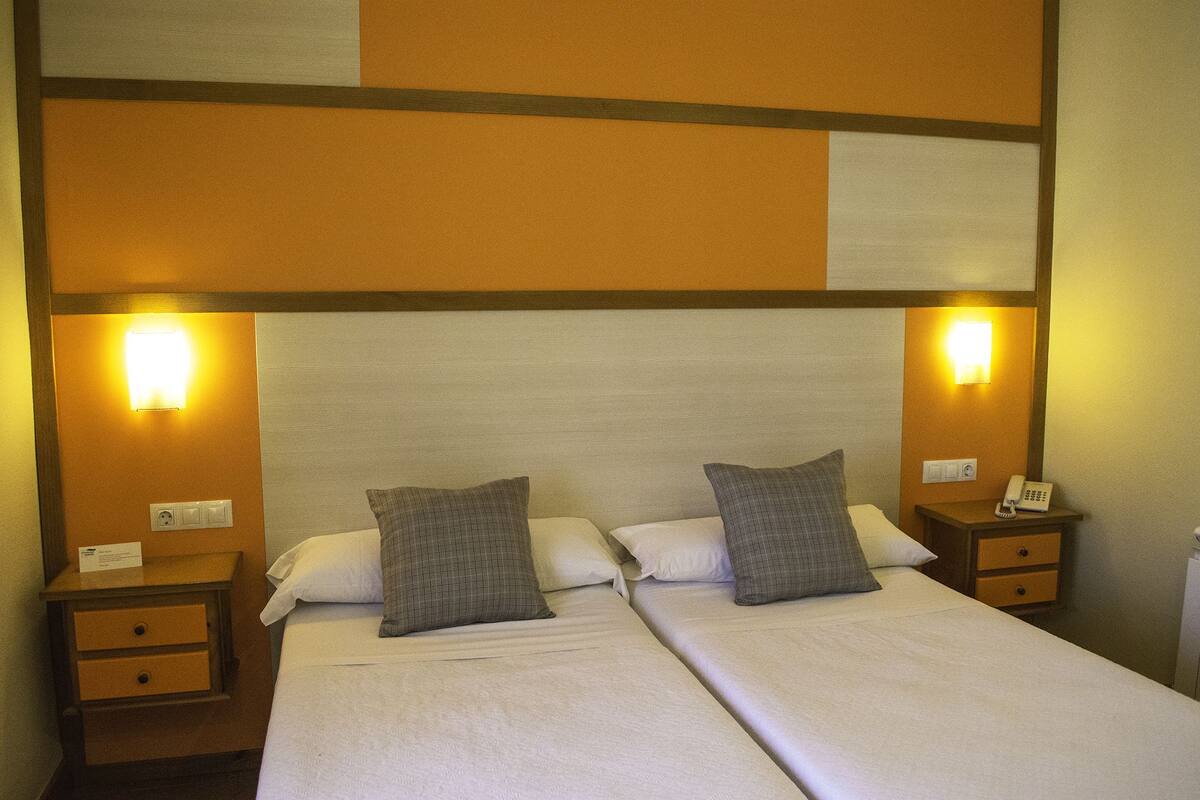 Una cama doble con dos almohadas, dos mesitas de noche con lámparas, y una pared con diseño geométrico.