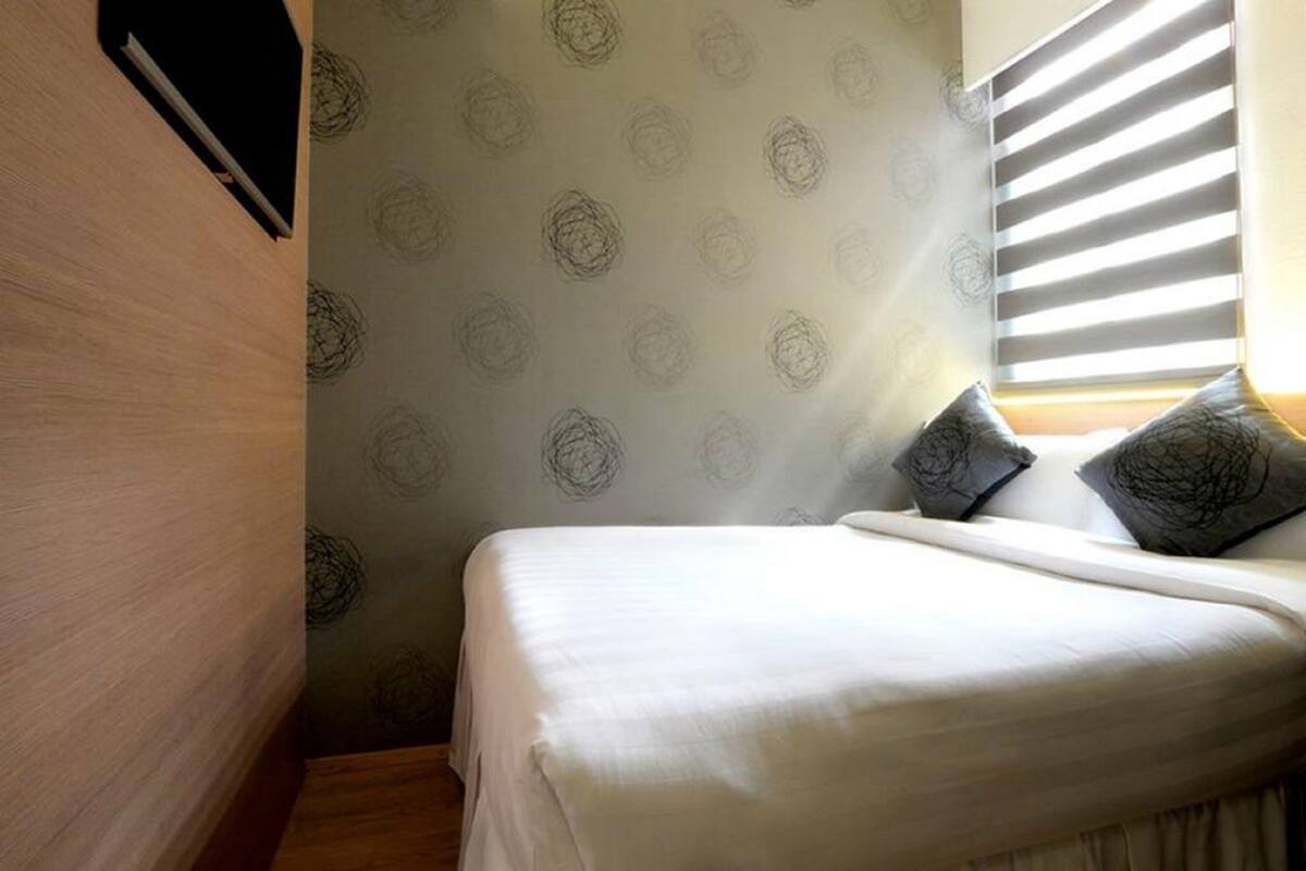 Ein kleines, gemütliches Schlafzimmer mit einem Bett, Kissen und einem Fenster mit Jalousien.