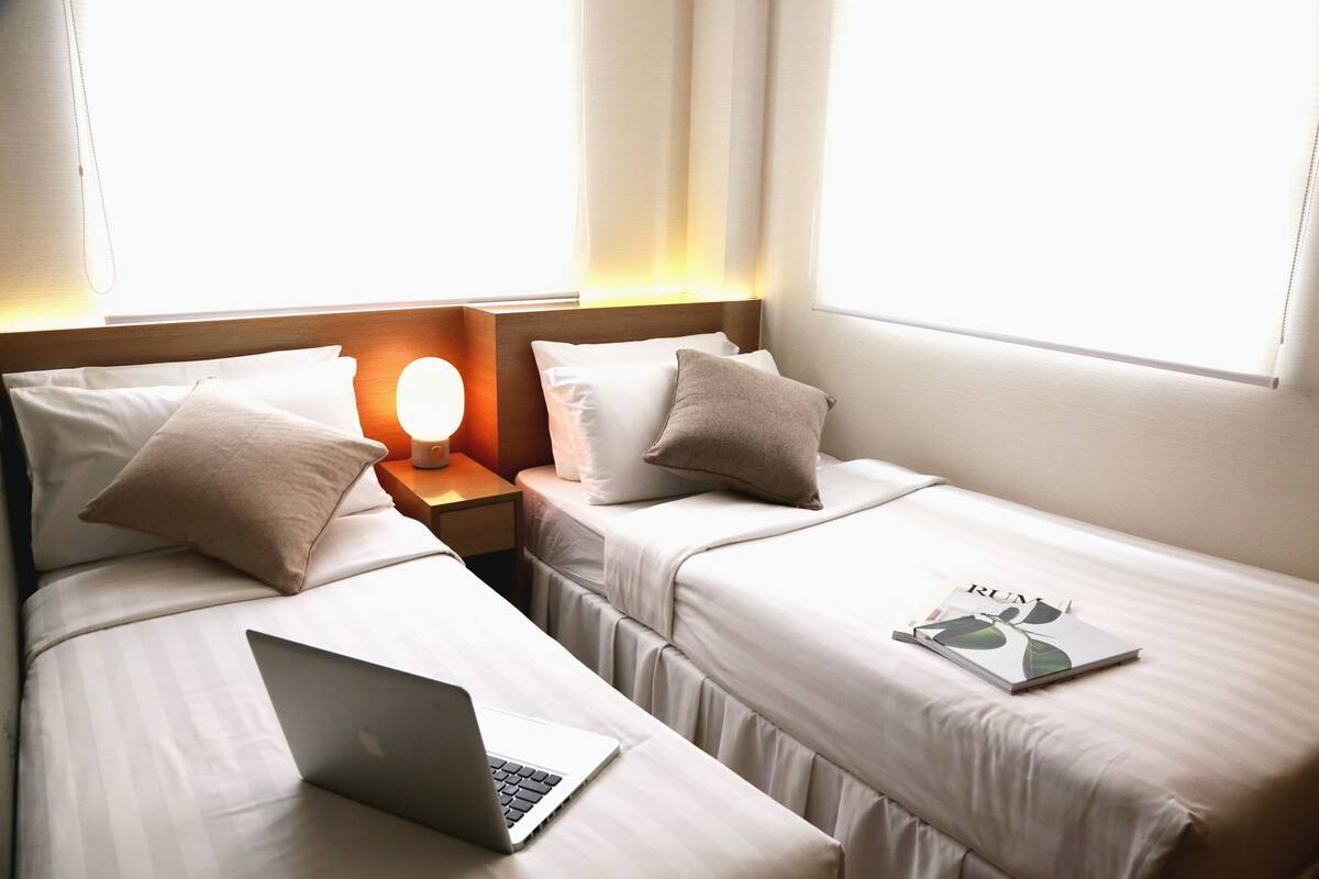 Ein Hotelzimmer mit zwei Betten, einem Nachttisch mit Lampe und einem Laptop auf einem Bett.