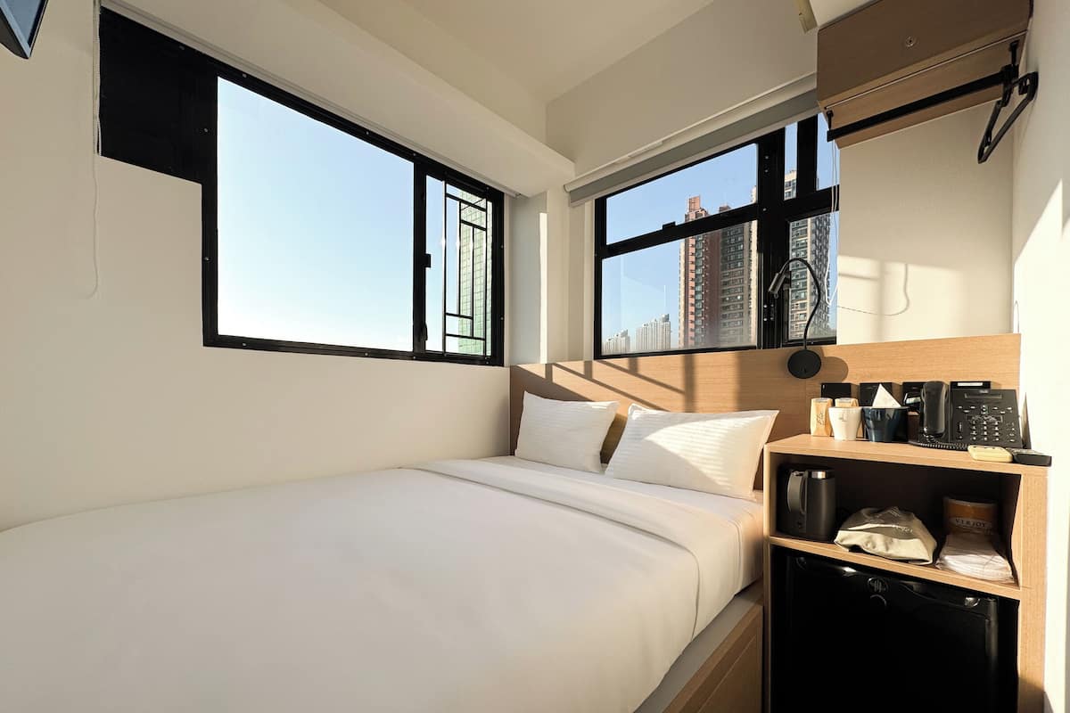 Ein Hotelzimmer mit Bett, Schreibtisch mit Telefon und Blick auf hohe Gebäude.