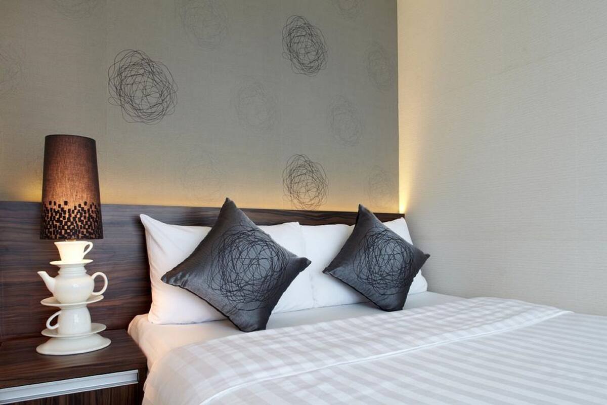 Ein Hotelzimmer mit einem Bett, zwei Kissen mit einem besonderen Design, einem Nachttisch mit Lampe und einer Wand mit dezentem Muster.