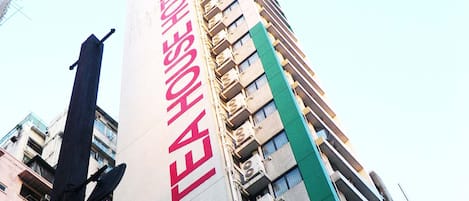 A tall building with a prominent vertical sign displaying a hotel name and contact number.