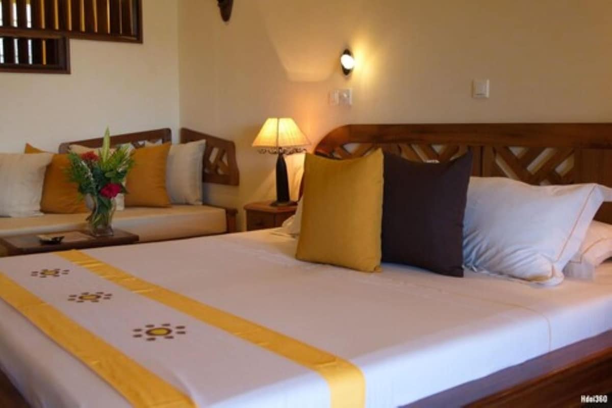 A hotel room with a large bed, a bedside table, a lamp, and a wall-mounted light.