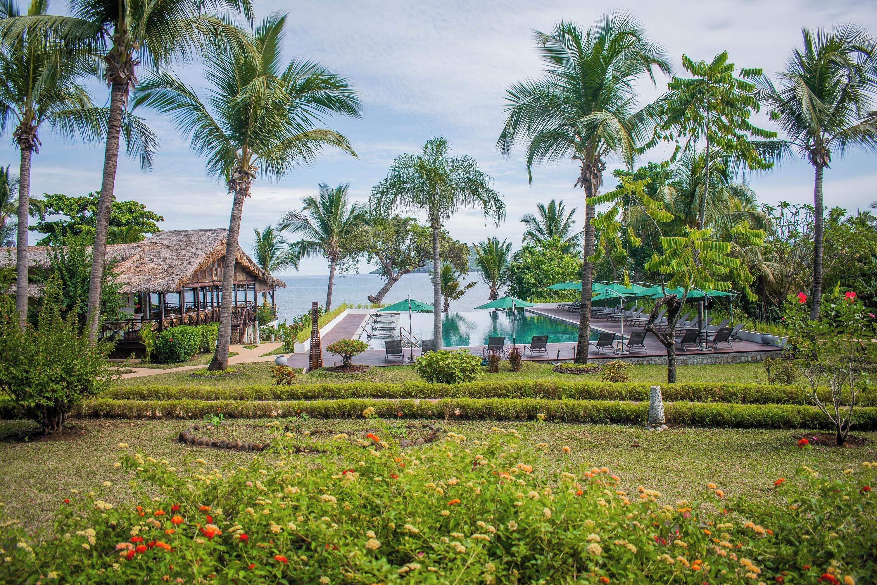 Ein Resort mit Pool, Palmen und einem Gebäude mit einem Reetdach.